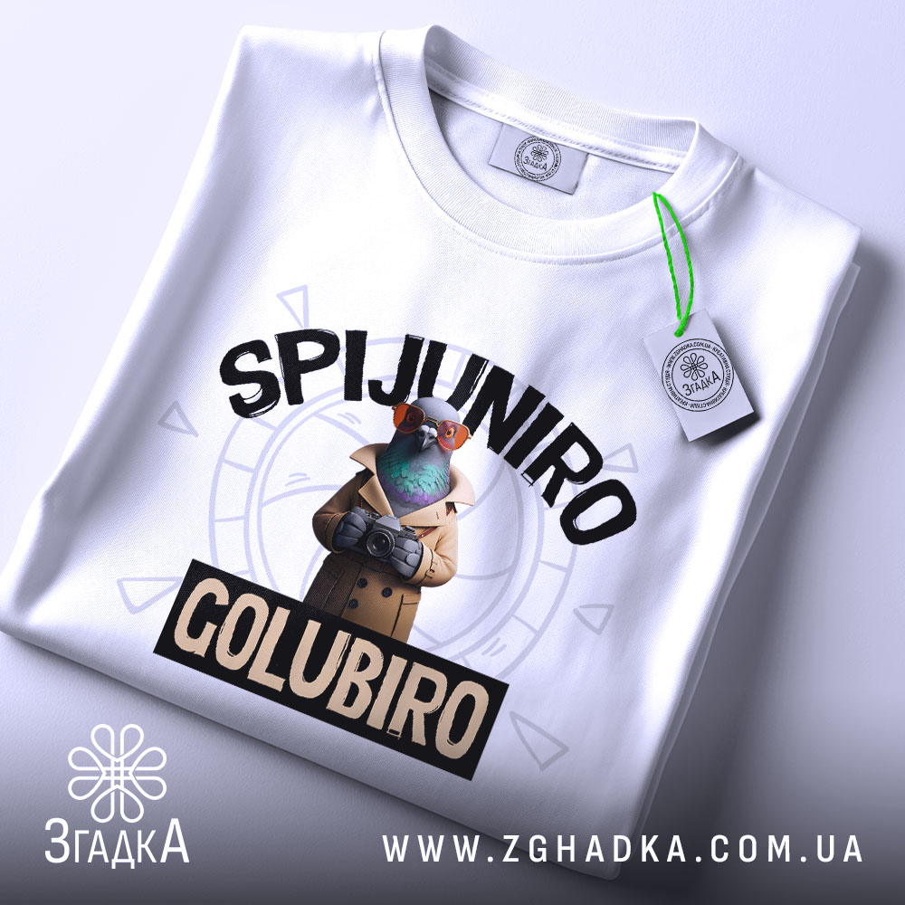 Футболка Spijuniro Golubiro білого кольору, зображена зверху, на столі, фон світло-сірий, принт з пташкою в окулярах та плащі, текст 'SPIJUNIRO' зверху та 'GOLUBIRO' внизу, на футболці є етикетка.