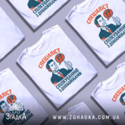 Футболка спілкування з довбойобами, біла, зображена на манекені, фон світло-сірий, принт з чоловіком у навушниках, який піднімає великий палець, текст червоного та зеленого кольорів.