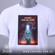 Футболка спокійно вони летять, біла, складена на поверхні, з видимим етикеткою, фон світлий, принт з зеленим інопланетянином, який показує знак миру, під космічним кораблем, оточеним зірками та планетами.