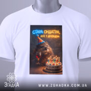 Футболка стара ондатра, біла, зображена з верхнього ракурсу, на фоні світлого градієнта, принт з ведмедем у святковому капелюшку, що тримає келих з вином, поряд з тортом з свічками, на комірці є етикетка.