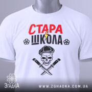 Футболка стара школа, біла, складена на поверхні, фон світлий, принт з червоним написом 'СТАРА' та чорним 'ШКОЛА', зображення черепа з капелюхом та ножами, на футболці є етикетка.