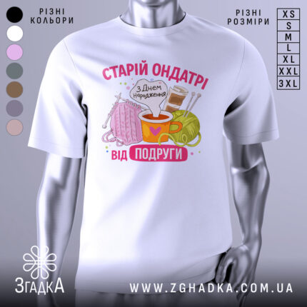Футболка старій ондатрі білого кольору, зображена з фронтального ракурсу на манекені, фон світло-сірий. Принт містить малюнки пряжі, чашки з напоєм та спиць, текст 'З Днем народження від подруги' у яскравих кольорах.