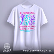 Футболка стоматолог білого кольору, підвішена на вішалці, фон світло-сірий, принт з текстом "Я - стоматолог. Ваша усмішка - мій автограф" у яскравих кольорах, з малюнком зуба та зубної щітки, виглядає стильно.