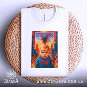 Футболка Stop War арт, біла, складена на плетеній кошику, фон світло-сірий, принт з зображенням дитини з серйозним виразом обличчя, на фоні вогню та будівель, текст "STOP WAR" у верхній частині принта.