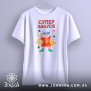 Футболка супер бабуся білого кольору, підвішена на вішалці, фон градієнтний сірий, принт з бабусею в червоному костюмі супергероя з синіми окулярами, текст 'СУПЕР БАБУСЯ' яскраво червоний, зірочки навколо принта.