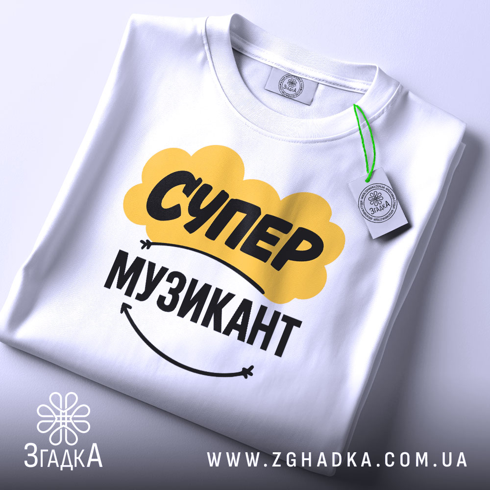 Футболка супер музикант, біла, складена на столі, фон світло-сірий, принт жовтого кольору з написом "СУПЕР" та чорного з написом "МУЗИКАНТ", на комірці є етикетка.