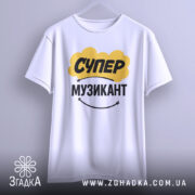 Футболка супер музикант, біла, підвішена на вішалці, фон світло-сірий, принт жовтого кольору з написом "СУПЕР" та чорного з написом "МУЗИКАНТ", під принтом є усміхнений смайлик.