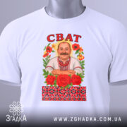 Футболка сват білого кольору, складена на столі, фон світло-сірий, принт з чоловіком у вишиванці, оточеним червоними трояндами та кольоровими квітами, напис 'СВАТ' зверху, на футболці є етикетка з зеленим шнурком.