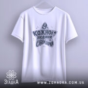 Футболка свої зірки. Біла футболка з коротким рукавом, підвішена на вішалці. Фон світло-сірий, принт у формі зірки з текстом "У кожної людини свої зірки" у темно-сірому кольорі.