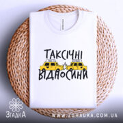 Футболка таксічні відносини, білого кольору, складена на плетеній основі, фон світло-сірий, принт з жовтими таксі та чорним текстом.