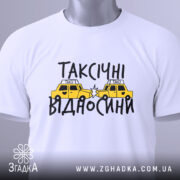 Футболка таксічні відносини, білого кольору, складена на столі, фон світло-сірий, принт з жовтими таксі та чорним текстом, з зеленим ярликом.