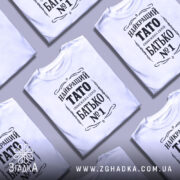 Футболка тато білого кольору, зображена на манекені з правого боку, фон світло-сірий, принт чорного кольору з написом 'НАЙКРАЩИЙ ТАТО ОБМЕЖЕНА СЕРІЯ БАТЬКО №1'.