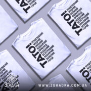 Футболка тато білого кольору, зображена на манекені з правого боку, фон світло-сірий, принт чорного кольору з написом 'TATO!' та переліком позитивних якостей тата.