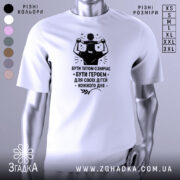 Футболка тато білого кольору, зображена з правого ракурсу на манекені, фон світло-сірий, принт чорного кольору з написом 'БУТИ ТАТОМ ОЗНАЧАЄ БУТИ ГЕРОЄМ ДЛЯ СВОЇХ ДІТЕЙ КОЖНОГО ДНЯ' та зображенням батька з дитиною на плечах.