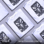 Футболка темна маска, біла, зображена на манекені з правого боку, фон світло-сірий, принт з чорним малюнком маски та черепами внизу.