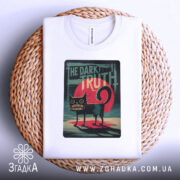 Футболка темна правда, біла, складена на плетеному кошику, фон світло-сірий, принт з чорним котом на червоному фоні з написом 'THE DARK TRUTH'.