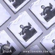 Футболка темний романтик, біла, зображена на манекені, з принтом чорного персонажа, що робить жест серця, на фоні автомобіля.