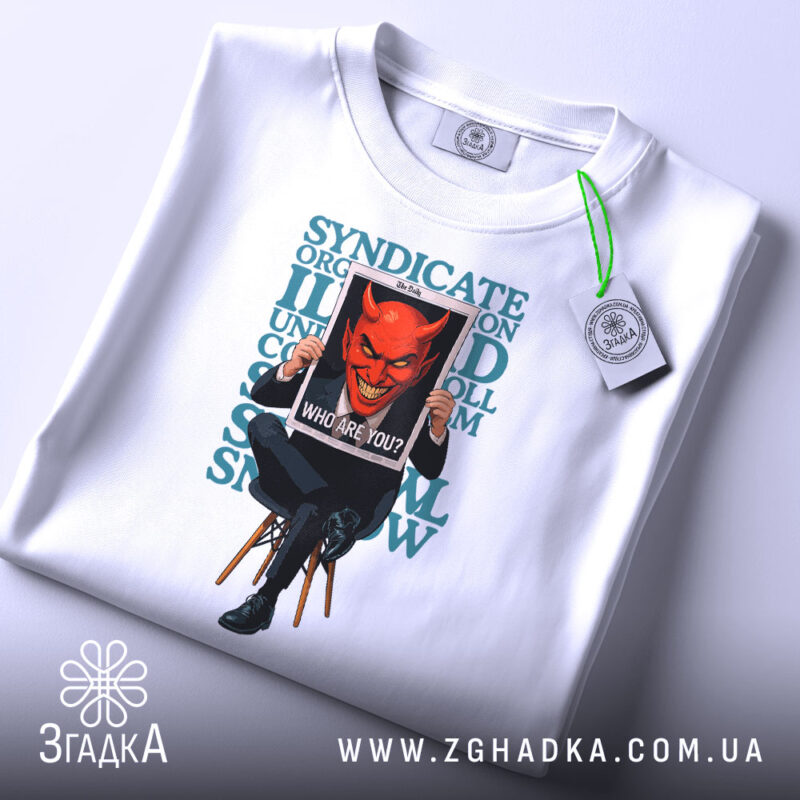 Футболка темний символізм, біла, складена на столі, фон світло-сірий, принт з червоним демоном, що тримає табличку з написом 'WHO ARE YOU?' на чорному фоні, текст на футболці у зелених тонах, з етикеткою з зеленим шнурком.