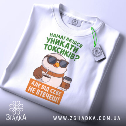Футболка токсик білого кольору, зображена зверху, на фоні світло-сірого кольору, принт з птахом у сонцезахисних окулярах, що тримає каву, текст зеленого та оранжевого кольорів, з етикеткою на комірці.