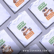 Футболка токсик білого кольору, зображена з фронтального ракурсу на манекені, фон світло-сірий, принт з веселим птахом у сонцезахисних окулярах, що тримає каву, текст зеленого та оранжевого кольорів.