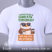 Футболка токсик білого кольору, зображена зверху, на фоні світло-сірого кольору, принт з птахом у сонцезахисних окулярах, що тримає каву, текст зеленого та оранжевого кольорів, з етикеткою на комірці.
