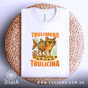 Футболка Trulimero Trulicina білого кольору, складена на плетеному кошику, фон білий, принт з котом у сонцезахисних окулярах і риб'ячим тілом, оточений зеленими рослинами, текст 'TRULIMERO TRULICINA' яскраво-оранжевого кольору.