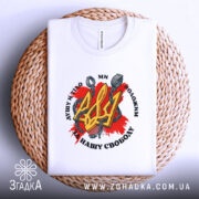 Футболка Тризуб і кайдани, біла, зображена зверху на плетеній кошику, фон світло-сірий, принт з червоним фоном, жовтим тризубом і кайданами, текст чорного кольору.