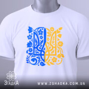 Футболка тризуб український орнамент, біла, зображена зверху, складена на столі, фон світло-сірий, принт у синьо-жовтих тонах з квітковими елементами, на комірці є етикетка.