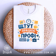 Футболка тут працює профі. Біла футболка, складена на плетеному кошику, фон світло-сірий. Принт яскравий, з елементами, що символізують роботу, такими як графіки та офісні предмети.