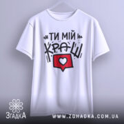 Футболка ти мій краш, білого кольору, зображена з фронтального ракурсу на вішалці, фон світло-сірий, принт містить текст "ТИ МІЙ КРАШ" у чорному кольорі та червоний коментар з серцем.