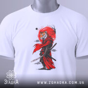 Футболка Тигр самурай воїн, біла, зображена на столі, фон світло-сірий, принт з тигром у червоному плащі, на футболці є етикетка з зеленим шнурком.