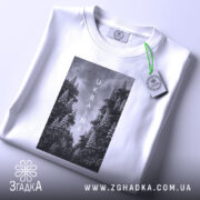 Футболка Ukraine білого кольору, складена на поверхні, з видимим етикеткою, фон світло-сірий, принт з чорнобілими зображеннями дерев та написом 'UKRAINE' по центру.