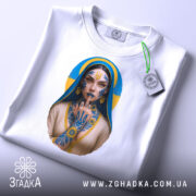 Футболка українська тату, біла, складена на столі, фон світло-сірий, принт з зображенням дівчини з татуюваннями, на футболці є етикетка з зеленим шнурком.