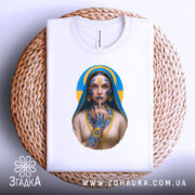 Футболка українська тату, біла, складена на плетеній кошику, фон світлий, принт з зображенням дівчини з татуюваннями, яка тримає палець на губах, з синьо-жовтим фоном.