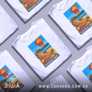 Футболка український настрій, біла, зображена на манекені, фон світло-сірий, принт з котом у сонцезахисних окулярах, що сидить на шезлонгу з напоєм, на фоні пляжу та вибуху.