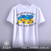 Футболка українці як бджоли, білого кольору, підвішена на вішалці, фон світло-сірий, принт з жовто-блакитними кольорами, бджолами та написом 'Краще їх не чіпати'.