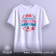 Футболка вчитель у світі білого кольору, підвішена на вішалці, фон світло-сірий, принт з текстом 'НАЙКРАЩИЙ ВЧИТЕЛЬ У СВІТІ' у рожевих та блакитних тонах, оточений елементами, такими як книга, дзвоник та ручка.