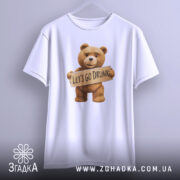 Футболка ведмедик let’s drunk, біла, підвішена на вішалці, фон світло-сірий, принт з ведмедиком, який тримає табличку з написом 'LET'S GO DRUNK'.