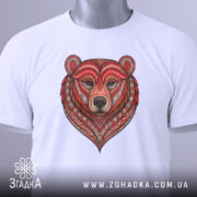 Футболка ведмідь білого кольору, складена на столі, фон світлий, принт ведмедя з червоними та коричневими деталями, на комірці прикріплена етикетка зеленого кольору.