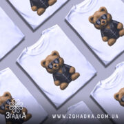 Футболка ведмідь патріот, біла, зображена на манекені, фон світло-сірий, принт ведмедя в чорній куртці та сонцезахисних окулярах з тризубом.