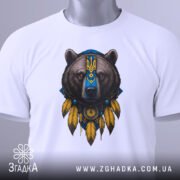 Футболка ведмідь символ, біла, складена на столі, фон світло-сірий, принт ведмедя з українським гербом, на комірці є етикетка.