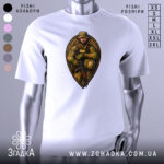 Футболка відважний воїн, білого кольору, зображена з фронтального ракурсу на манекені, фон світло-сірий, принт з військовим у камуфляжі, який тримає автомат, обрамлений декоративним елементом.