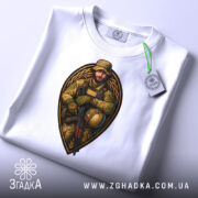 Футболка відважний воїн, білого кольору, зображена зверху на плоскому фоні, принт з військовим у камуфляжі, який тримає автомат, з етикеткою, що звисає з коміра.