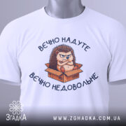 Футболка вєчно недовольне, білого кольору, зображена зверху, на ній видно принт з їжаком в коробці, фон світло-сірий, на комірці є етикетка.