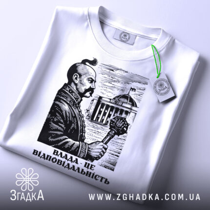 Футболка влада це відповідальність, біла футболка на столі, зображення чоловіка з вусами, що тримає скіпетр, на фоні будівлі, принт виконаний у чорному кольорі, з зеленим ярликом.