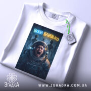 Футболка вони близько, біла, зображена на столі, фон світло-сірий, принт з космонавтом, який кричить, на фоні силуети прибульців і написом 'вони близько', з етикеткою на шнурку.