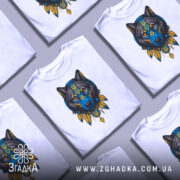 Футболка вовк білого кольору, зображена на манекені, з принтом вовка в синіх та жовтих тонах, фон світло-сірий, деталі принта включають тризуб та пір'я.