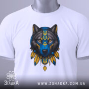 Футболка вовк білого кольору, складена на поверхні, з принтом вовка в синіх та жовтих тонах, вид з верхнього ракурсу, фон світло-сірий, на футболці є етикетка з зеленим шнурком.