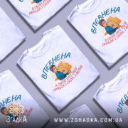 Футболка впевнена сильна жінка, білого кольору, зображена на манекені з правого боку, фон світло-сірий, принт з жінкою в синій блузці та червоній пов'язці, що демонструє силу, текст на українській мові.