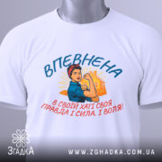 Футболка впевнена сильна жінка, білого кольору, зображена зверху, фон світло-сірий, принт з жінкою в синій блузці та червоній пов'язці, текст на українській мові, прикріплена етикетка з логотипом.